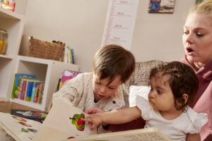 Comparing different forms of childcare in London doesn't have to take weeks. The image shows two small children and their childminder exploring a book together.