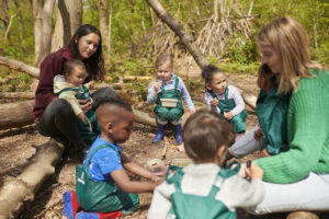 childminder who used to be a teacher teaches a class outside in the forest