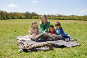 childminder reads book to children in the park