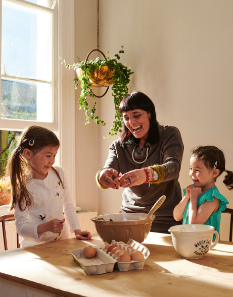An experienced nanny cooks with two young girls she's taking care of.