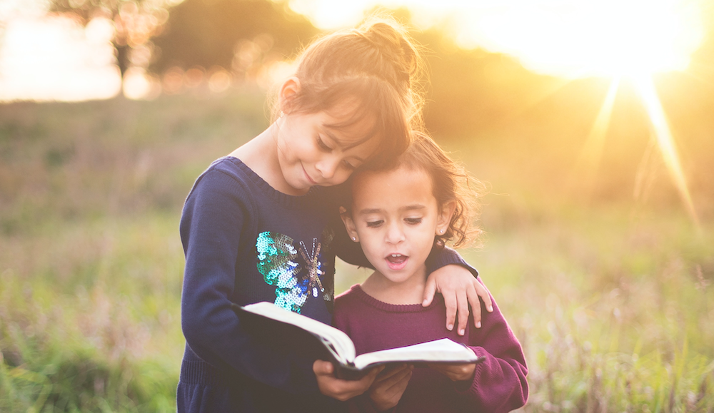two little children reading a book together outside