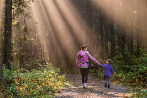 adult and child walking in a forest together with sunbeams coming through the trees