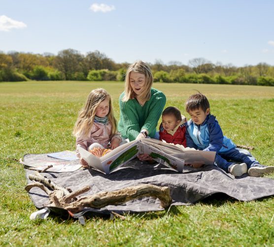 childminder reads book to children in the park