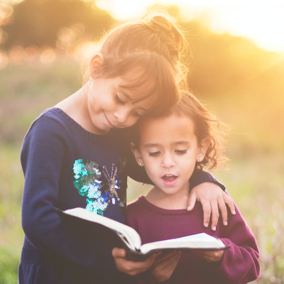 two little children reading a book together outside