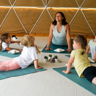 victoria tso demonstrating a yoga pose for kids with children on blue mats