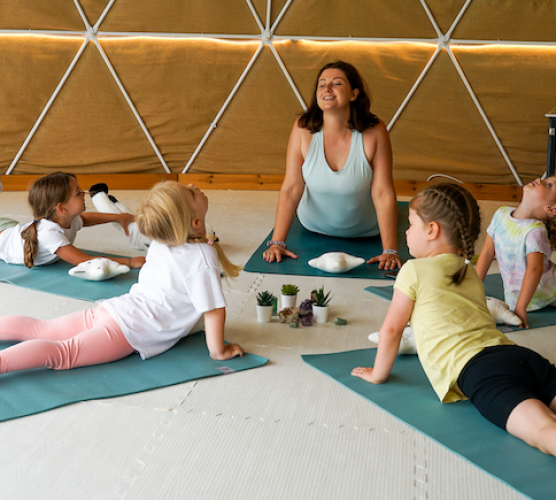 victoria tso demonstrating a yoga pose for kids with children on blue mats
